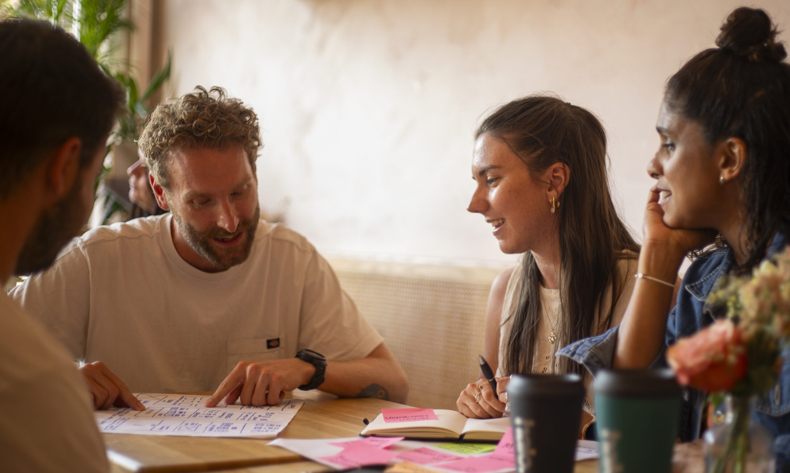 A diverse group of people gathered around a table, focused on a notebook as they exchange thoughts and ideas.