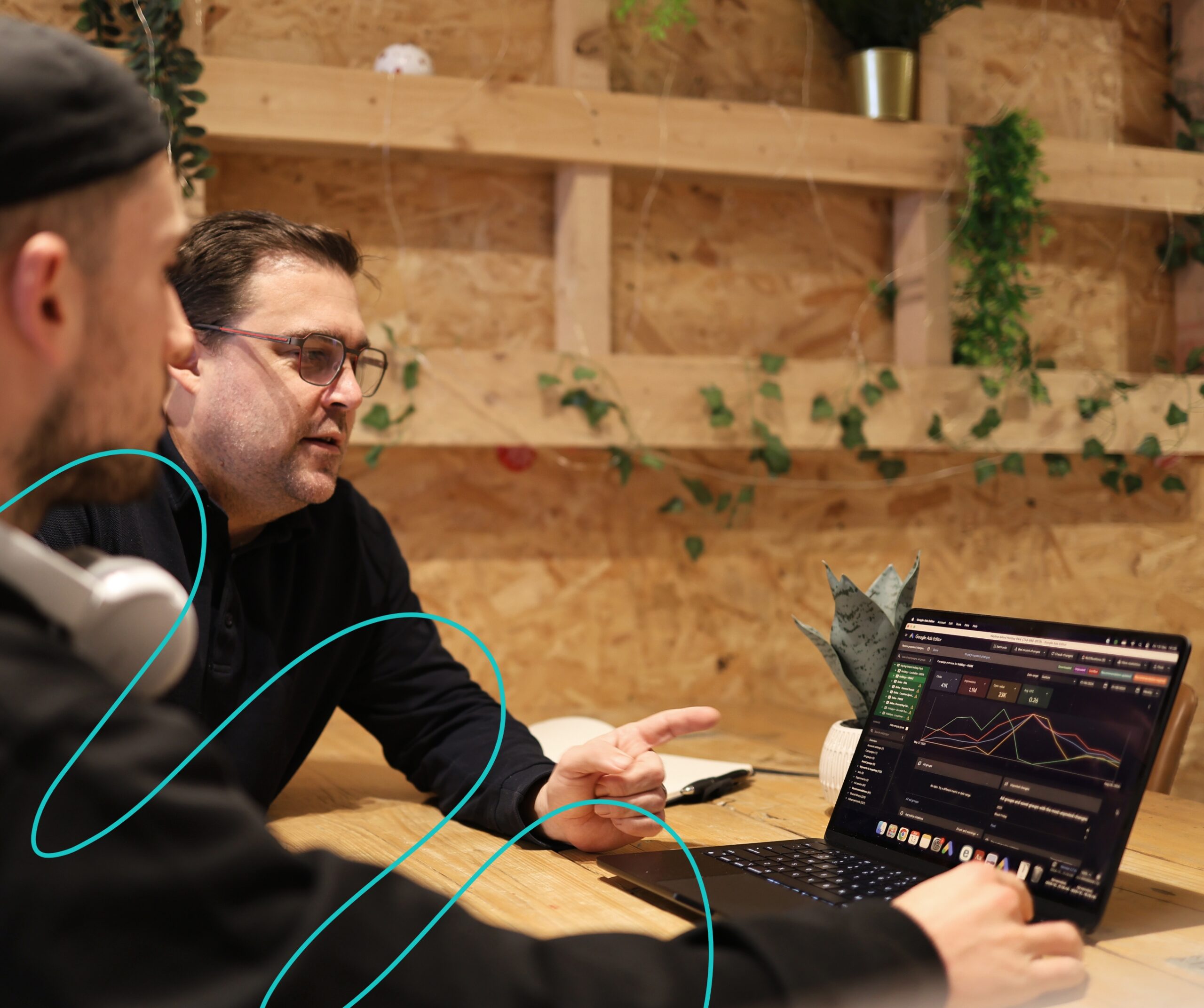 Two men engaged in discussion at a table, using a laptop for reference.