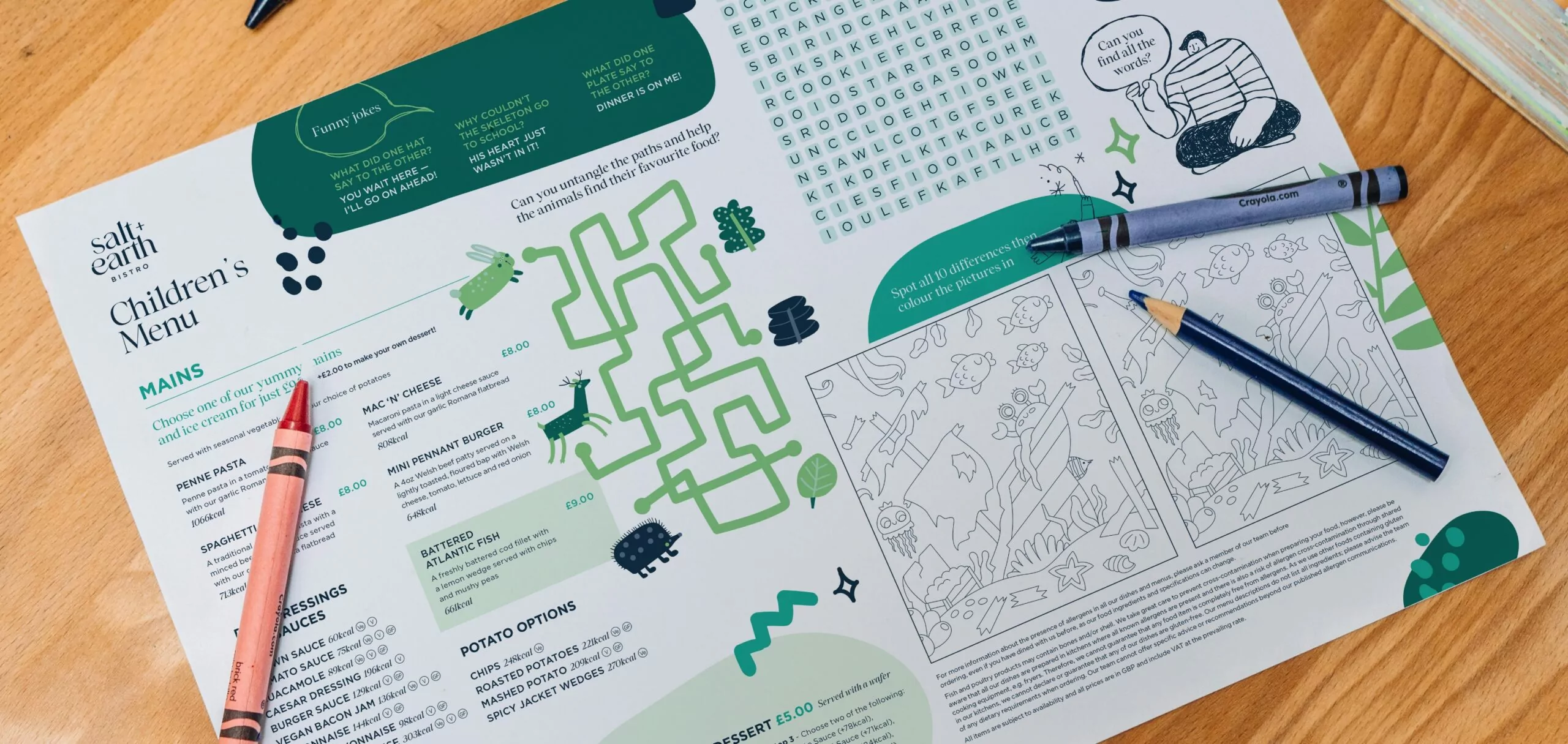 A fun and engaging children’s menu from Salt + Earth Bistro, featuring a selection of kid-friendly mains like penne pasta, mac ‘n’ cheese, and mini burgers. The menu includes interactive activities such as a maze, a word search, and a spot-the-difference game to keep children entertained. Crayons and a colored pencil are placed on the table, ready for use. The design incorporates playful green illustrations and a friendly layout, making it an inviting dining experience for families.