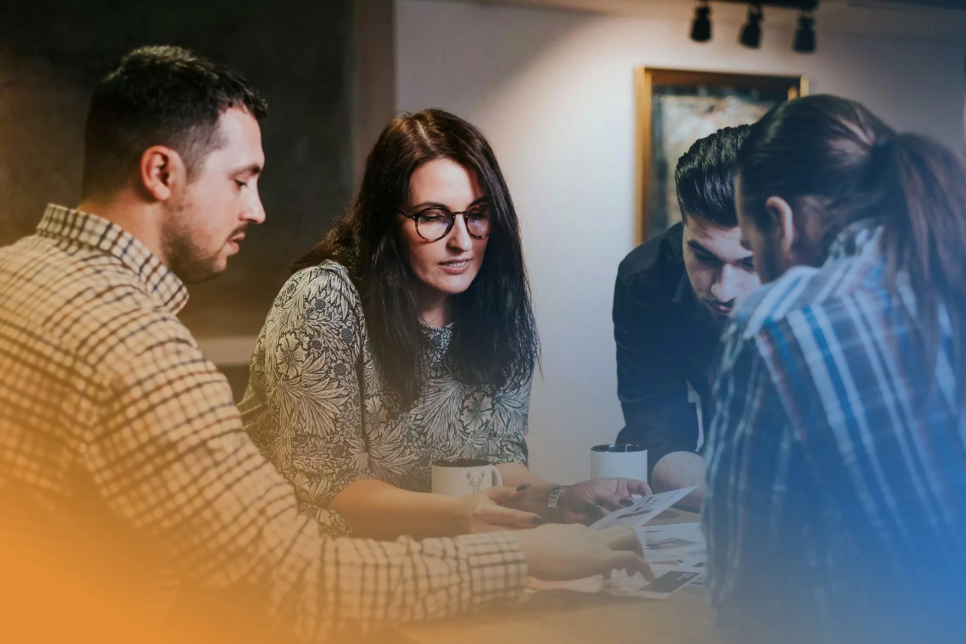 Four colleagues having a focused discussion around a table, reviewing printed materials in a modern office setting.