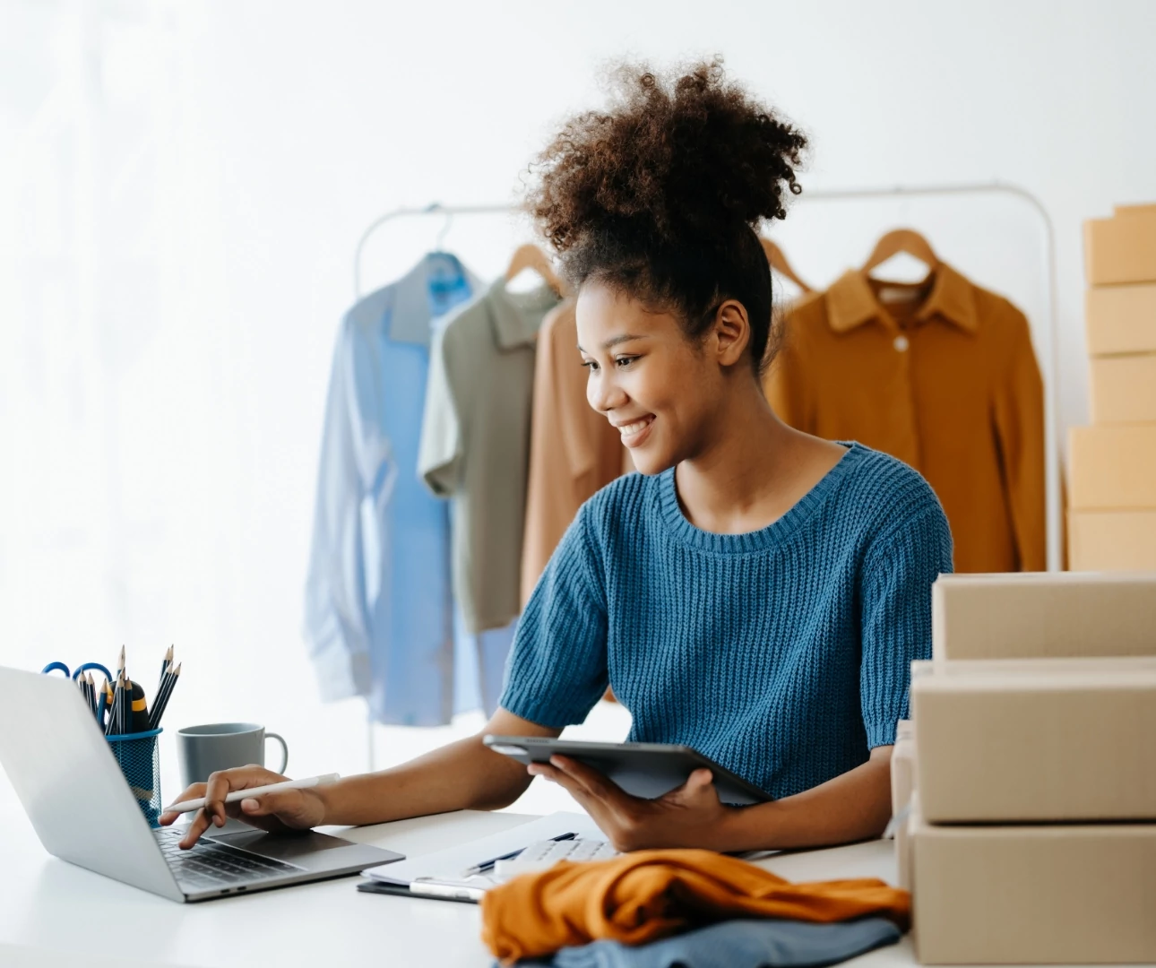 A woman at a desk with a laptop, surrounded by boxes, contemplating the right ecommerce platform for her business.