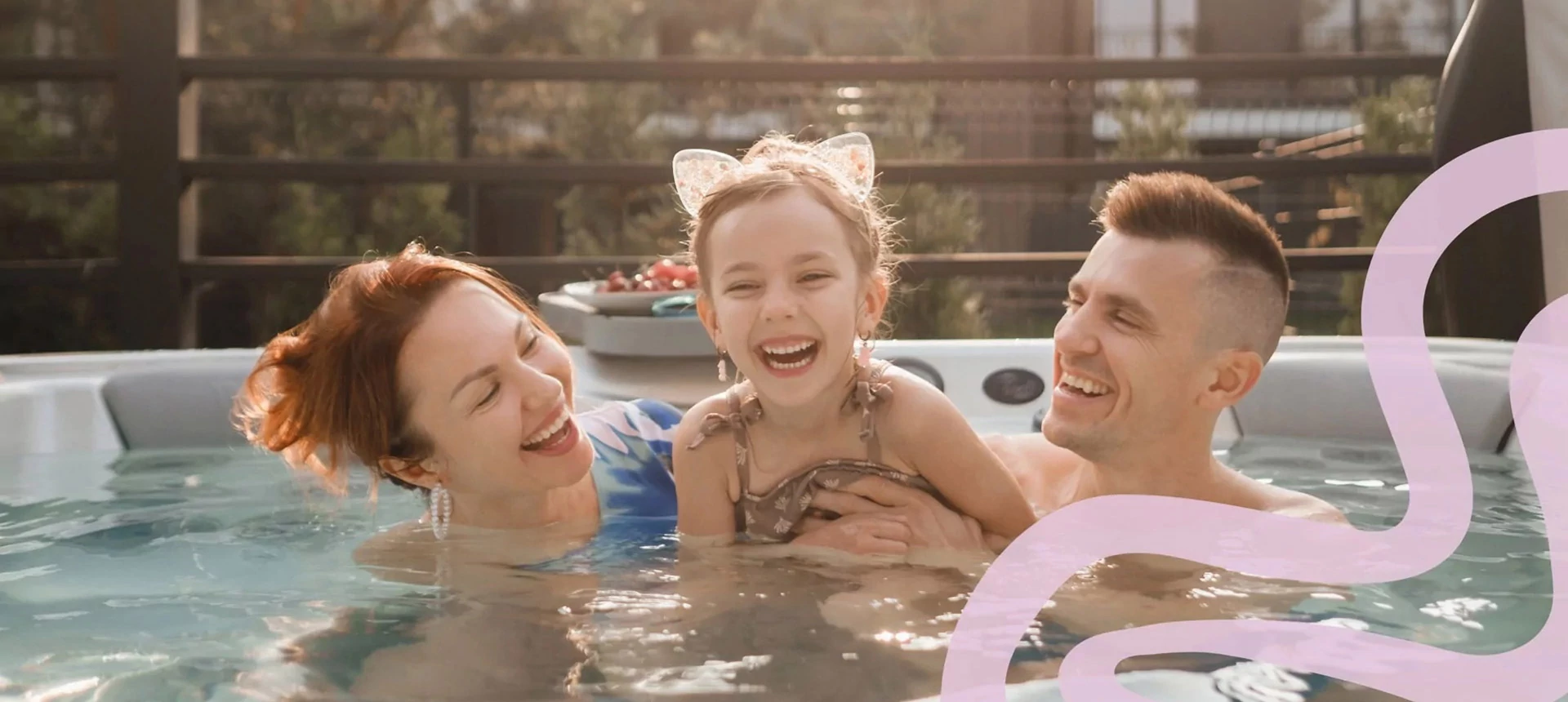 Happy family enjoying time together in an outdoor hot tub, with a young girl wearing cat ear headband laughing between her smiling parents.